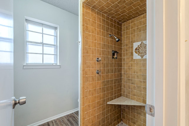 full bathroom featuring baseboards, wood finished floors, and a tile shower