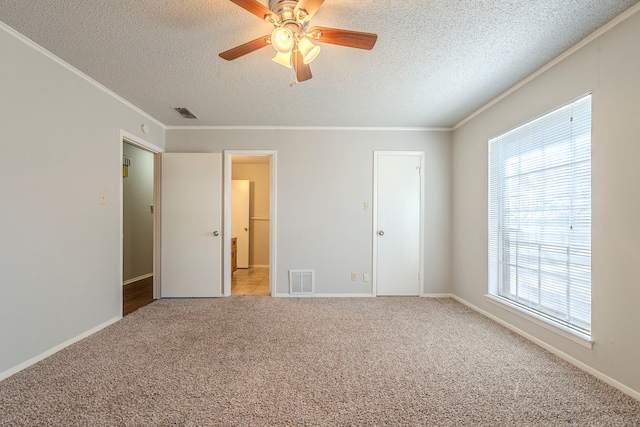 unfurnished bedroom with visible vents, light colored carpet, a textured ceiling, and ornamental molding