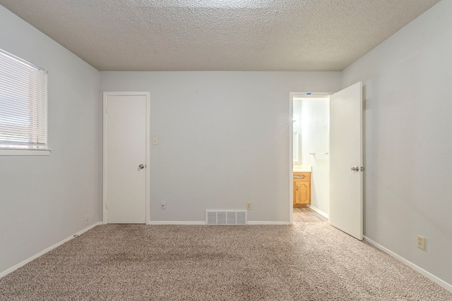 unfurnished bedroom featuring visible vents, baseboards, ensuite bath, a textured ceiling, and light colored carpet