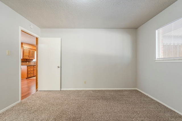 unfurnished room featuring light colored carpet, a textured ceiling, and baseboards