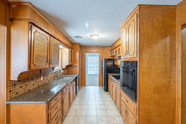 kitchen featuring dark stone counters, a sink, decorative backsplash, black appliances, and brown cabinets