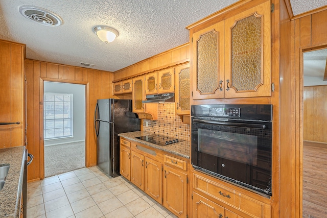 kitchen with visible vents, wooden walls, under cabinet range hood, brown cabinetry, and black appliances