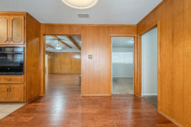 kitchen with wooden walls, visible vents, black oven, and ceiling fan
