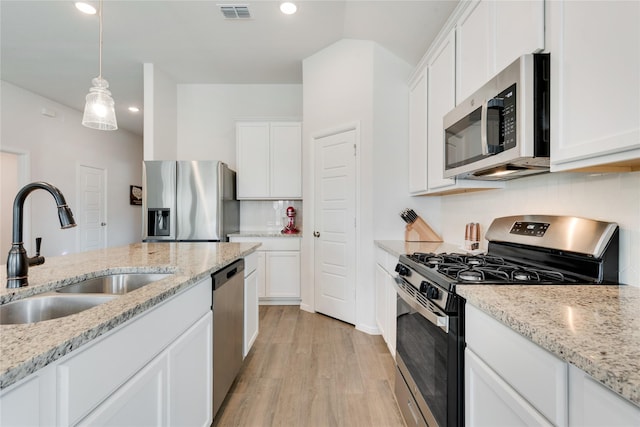 kitchen with decorative light fixtures, appliances with stainless steel finishes, light wood-style floors, white cabinetry, and a sink