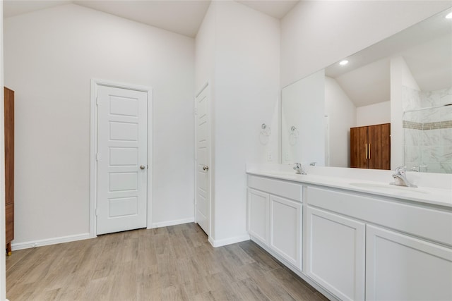 full bath featuring a sink, wood finished floors, vaulted ceiling, and a tile shower