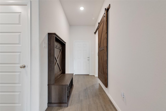 corridor with a barn door, light wood-style flooring, and baseboards