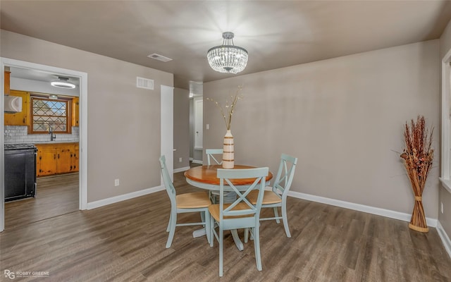 dining area featuring a chandelier, visible vents, baseboards, and wood finished floors