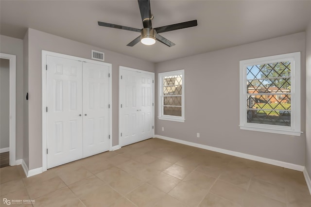 unfurnished bedroom with visible vents, baseboards, and two closets