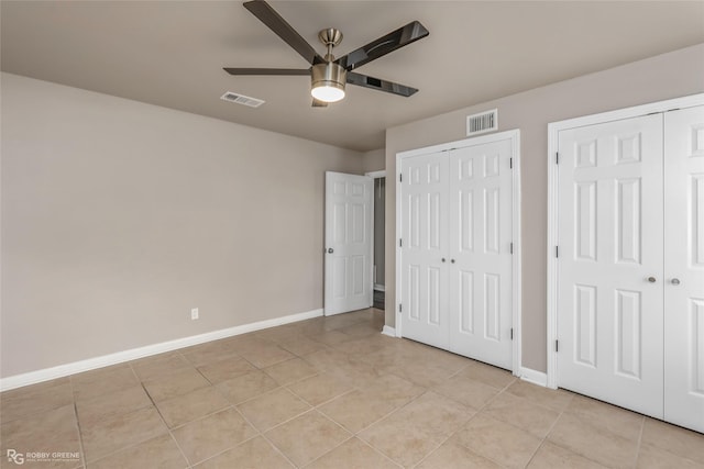 unfurnished bedroom featuring light tile patterned floors, visible vents, and multiple closets