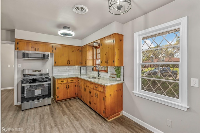 kitchen with visible vents, a sink, stainless steel appliances, tasteful backsplash, and light wood-type flooring