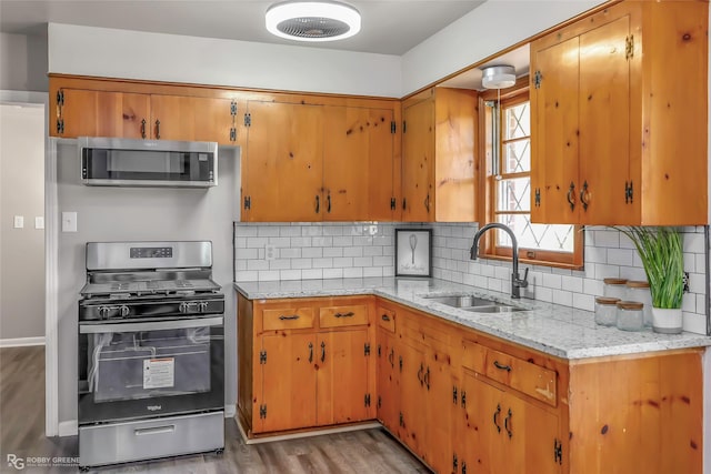 kitchen with a sink, tasteful backsplash, wood finished floors, appliances with stainless steel finishes, and light stone countertops