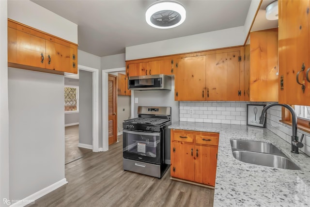 kitchen featuring brown cabinetry, light wood-style flooring, a sink, decorative backsplash, and appliances with stainless steel finishes