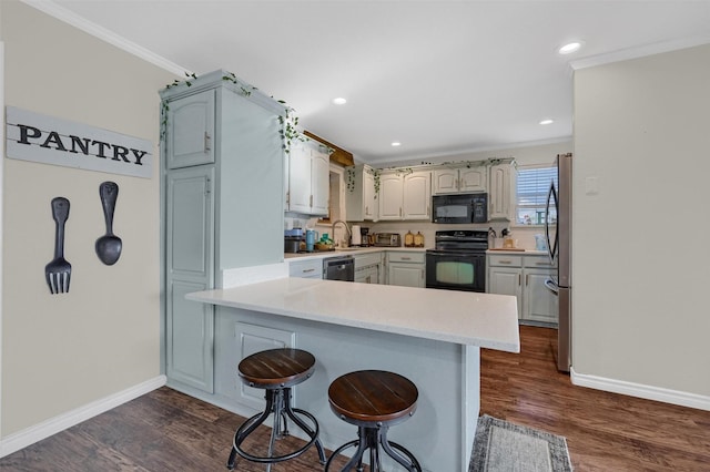 kitchen with dark wood finished floors, light countertops, ornamental molding, a peninsula, and black appliances