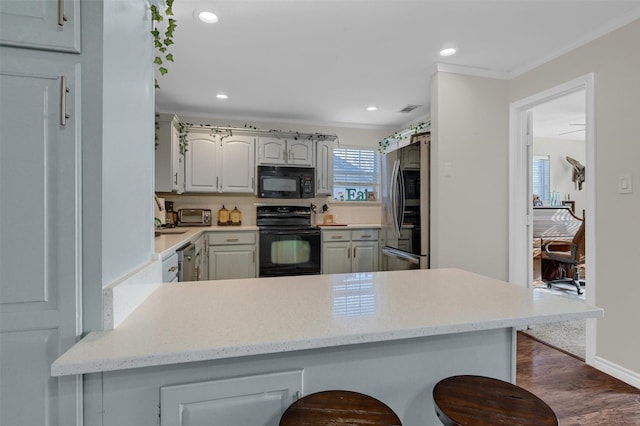 kitchen featuring recessed lighting, a peninsula, a kitchen breakfast bar, black appliances, and dark wood-style flooring