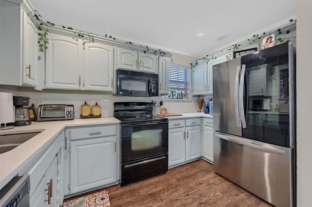 kitchen with tasteful backsplash, dark wood-type flooring, black appliances, and a toaster