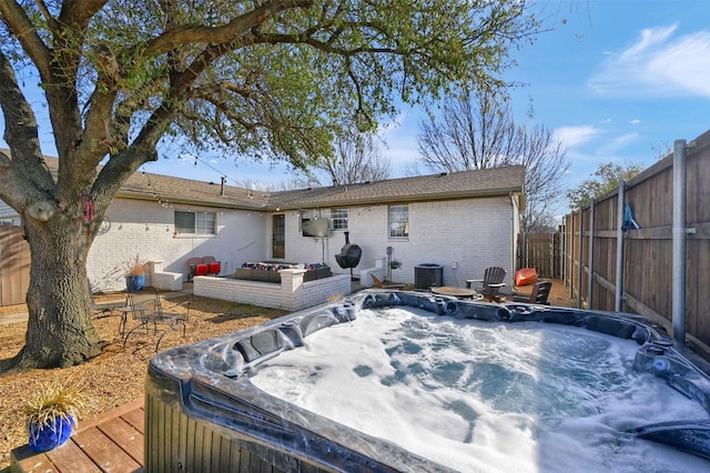 back of property featuring brick siding, a hot tub, and a fenced backyard
