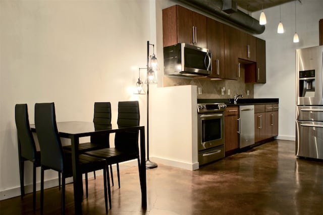 kitchen with decorative backsplash, baseboards, stainless steel appliances, dark countertops, and finished concrete floors