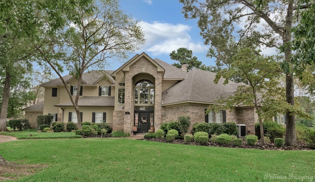 view of front of property with brick siding, a chimney, a shingled roof, and a front yard