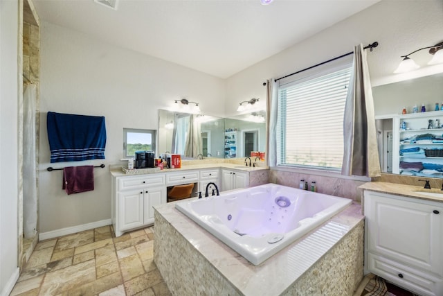bathroom featuring baseboards, a jetted tub, stone tile floors, and vanity