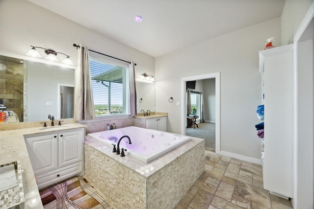 bathroom with a sink, two vanities, stone tile floors, and a bath