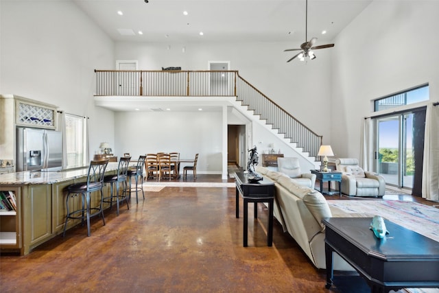 living area with finished concrete floors, recessed lighting, a high ceiling, ceiling fan, and stairs