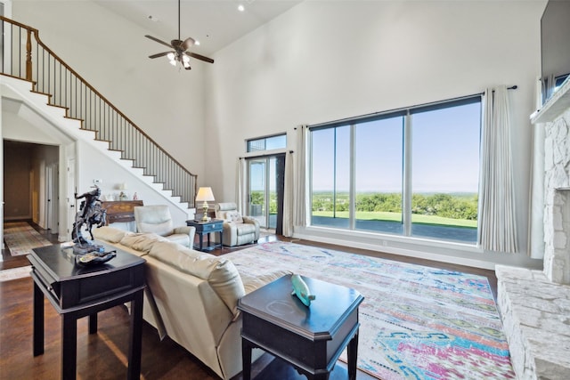 living area with a ceiling fan, stairway, wood finished floors, and a towering ceiling