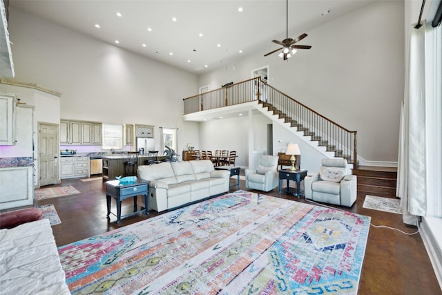 living room featuring a ceiling fan, recessed lighting, stairway, baseboards, and a towering ceiling