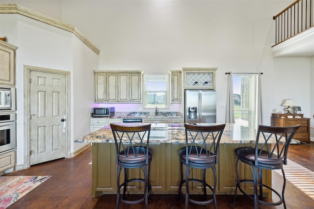 kitchen featuring light stone countertops, a high ceiling, dark wood-style flooring, stainless steel appliances, and cream cabinetry