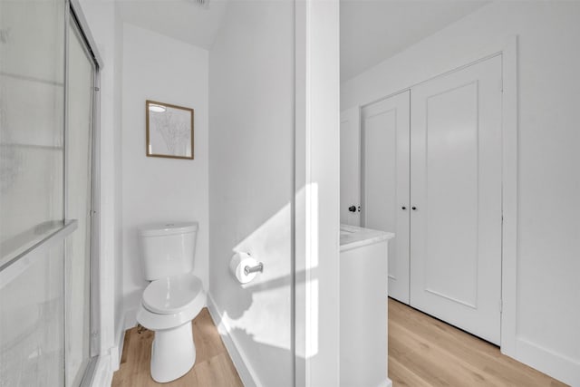 bathroom featuring toilet, a stall shower, wood finished floors, baseboards, and vanity