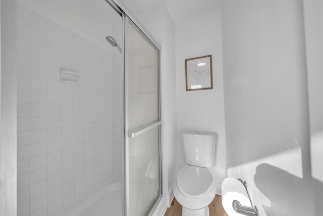 bathroom with a shower stall, toilet, and wood finished floors