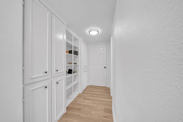 corridor with light wood-style floors and a textured wall