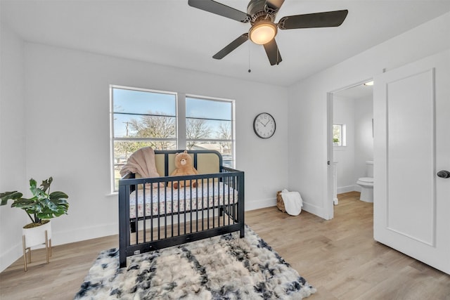 bedroom featuring a ceiling fan, a nursery area, light wood-style floors, and baseboards