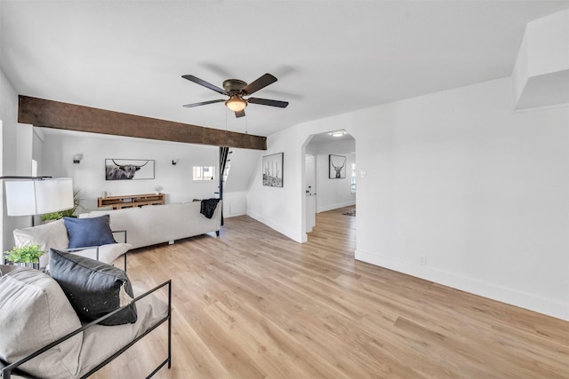 living area featuring light wood-style flooring, baseboards, arched walkways, and ceiling fan