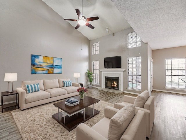 living area with baseboards, ceiling fan, a tile fireplace, wood finished floors, and a textured ceiling