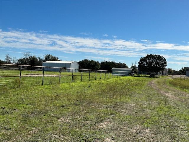 view of yard featuring an outbuilding, a rural view, and fence