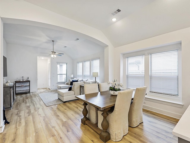 dining space with light wood-type flooring, vaulted ceiling, visible vents, and arched walkways