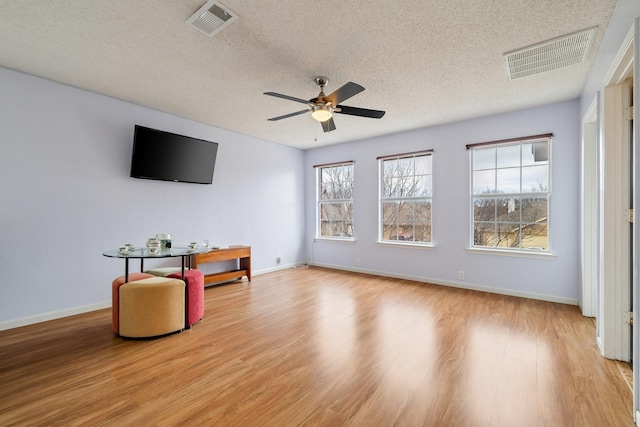 living room with a ceiling fan, light wood-style flooring, a textured ceiling, and visible vents