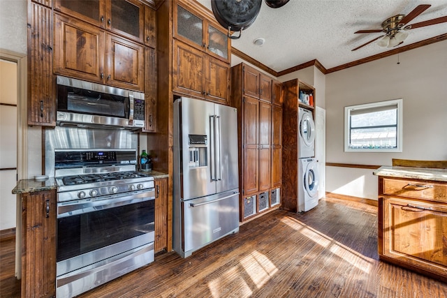 kitchen with ceiling fan, ornamental molding, stainless steel appliances, stacked washer and dryer, and a textured ceiling
