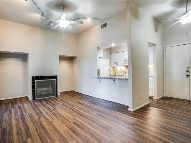 unfurnished living room with visible vents, dark wood-style floors, a ceiling fan, and a tiled fireplace