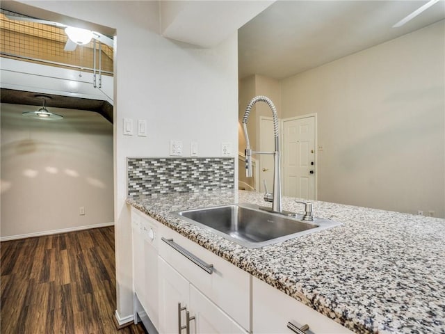 kitchen with a sink, light stone counters, dark wood finished floors, white cabinets, and white dishwasher
