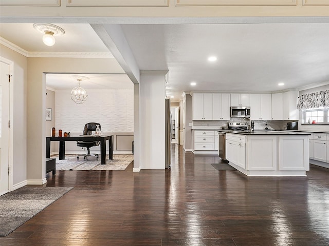 kitchen featuring appliances with stainless steel finishes, dark countertops, crown molding, dark wood-type flooring, and a desk