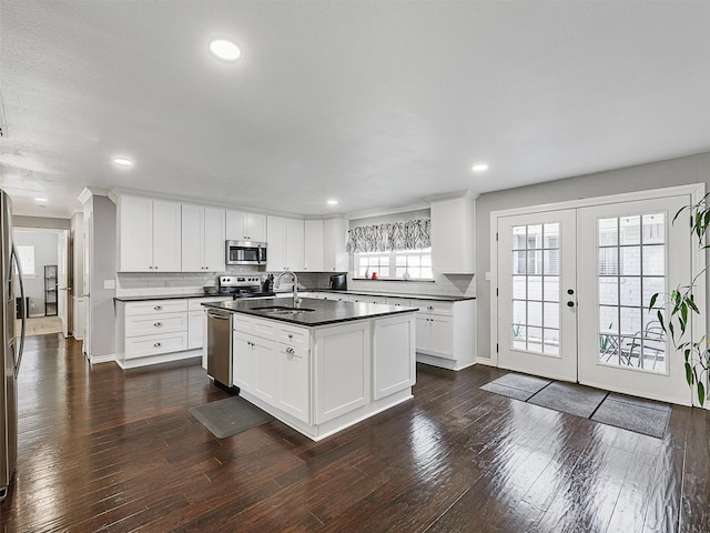 kitchen with stainless steel appliances, dark countertops, a sink, tasteful backsplash, and dark wood-style floors