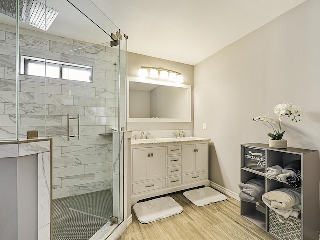 bathroom with a shower stall, wood finished floors, double vanity, baseboards, and a skylight