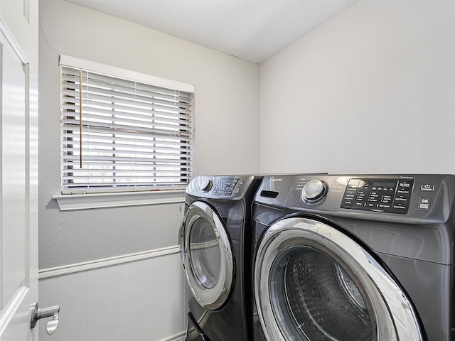 clothes washing area with washer and dryer and a wainscoted wall