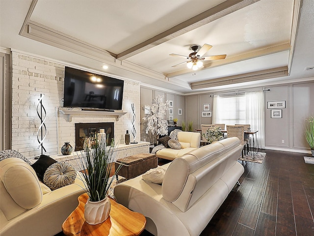 living room with dark wood finished floors, a brick fireplace, ceiling fan, crown molding, and a raised ceiling