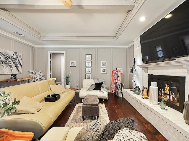 living room featuring a decorative wall, dark wood-style floors, ornamental molding, and a brick fireplace