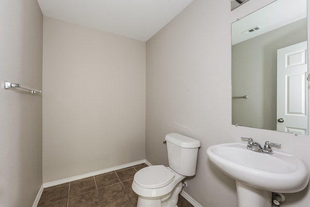 half bathroom with tile patterned floors, visible vents, toilet, a sink, and baseboards