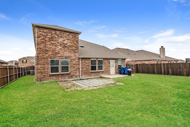 back of house featuring a fenced backyard, a lawn, brick siding, and roof with shingles