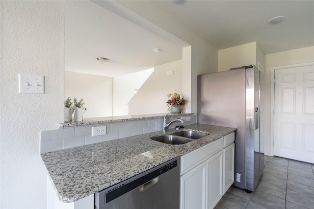 kitchen with light stone countertops, dishwasher, light tile patterned floors, white cabinetry, and a sink