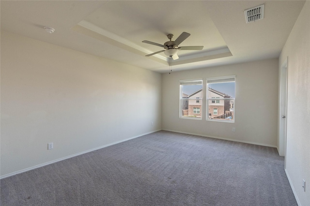 carpeted empty room featuring a tray ceiling, baseboards, visible vents, and ceiling fan